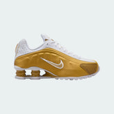 Nike Shox R4 Juniors' trainers in white and metallic gold, side profile showing the four visible Shox cushioning columns in the heel and a sleek upper with a gold Nike Swoosh.
